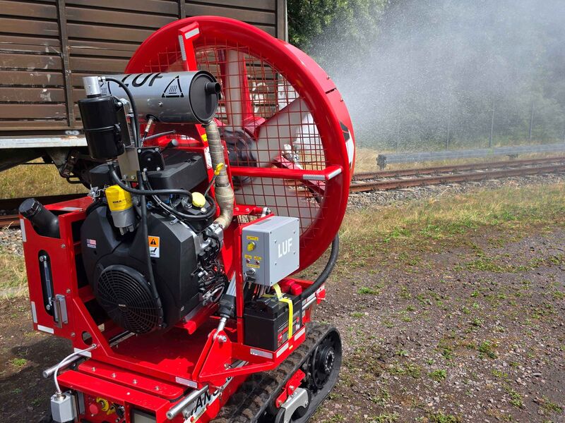 Ein ferngesteuerter Löschroboter mit einem großen Anbaugerät gibt aus der Rückansicht einen Wasserstrahl ab.