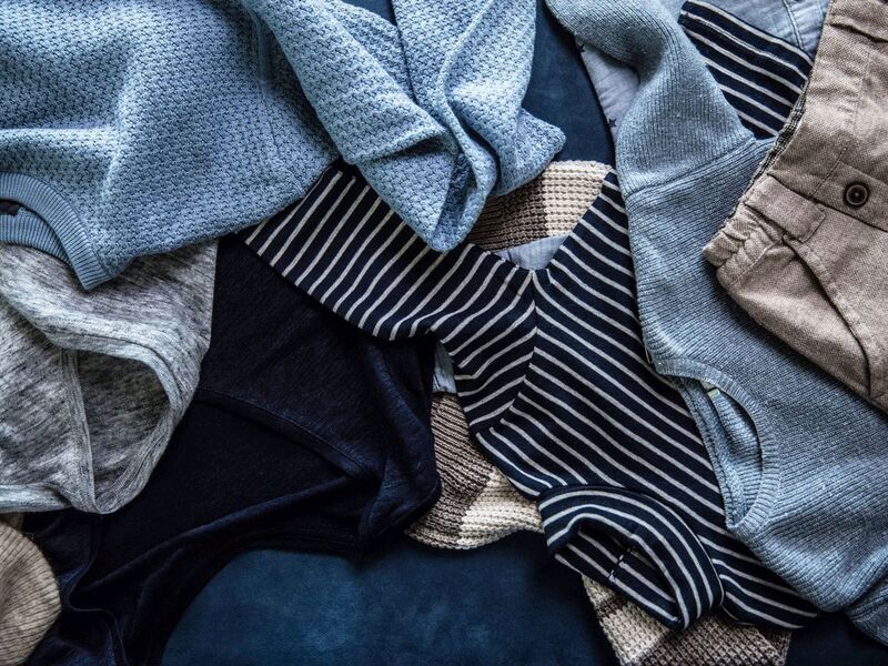 Verschiedene Kleidungsstücke, darunter blaue und gestreifte Pullover sowie eine blaue Hose, liegen übereinander.