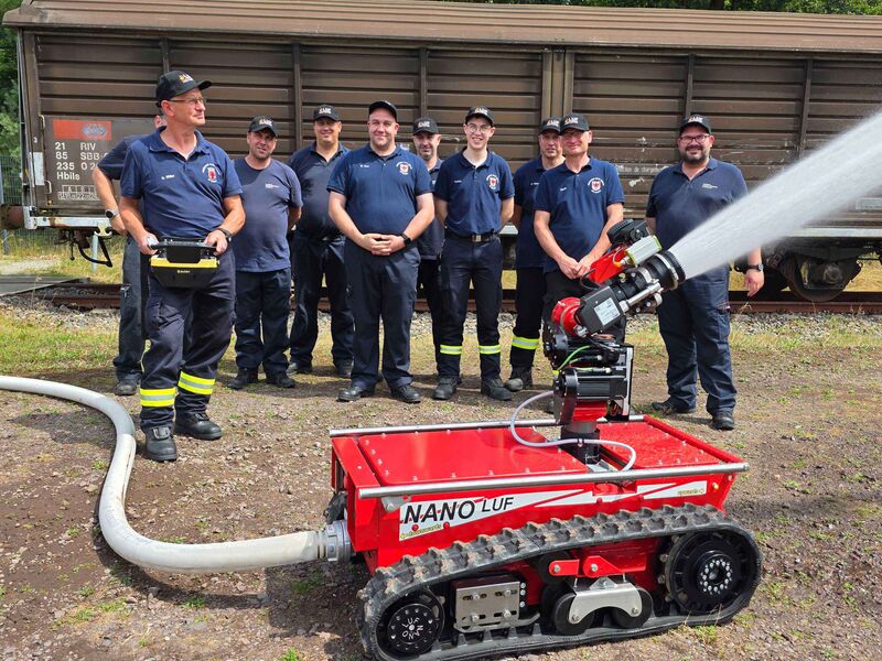 Mehrere Einsatzkräfte der Feuerwehr stehen hinter einem ferngesteuerten Löschroboter, aus dessen Löschdüse ein Wasserstrahl austritt.