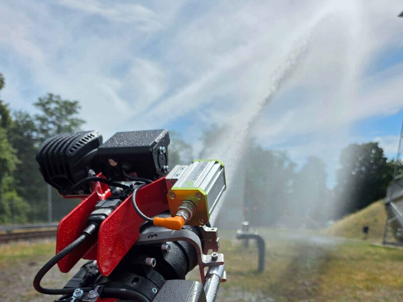 Die Löschdüse eines ferngesteuerten Löschroboters ist von hinten zu sehen und gibt einen Wasserstrahl auf eine Freifläche ab.