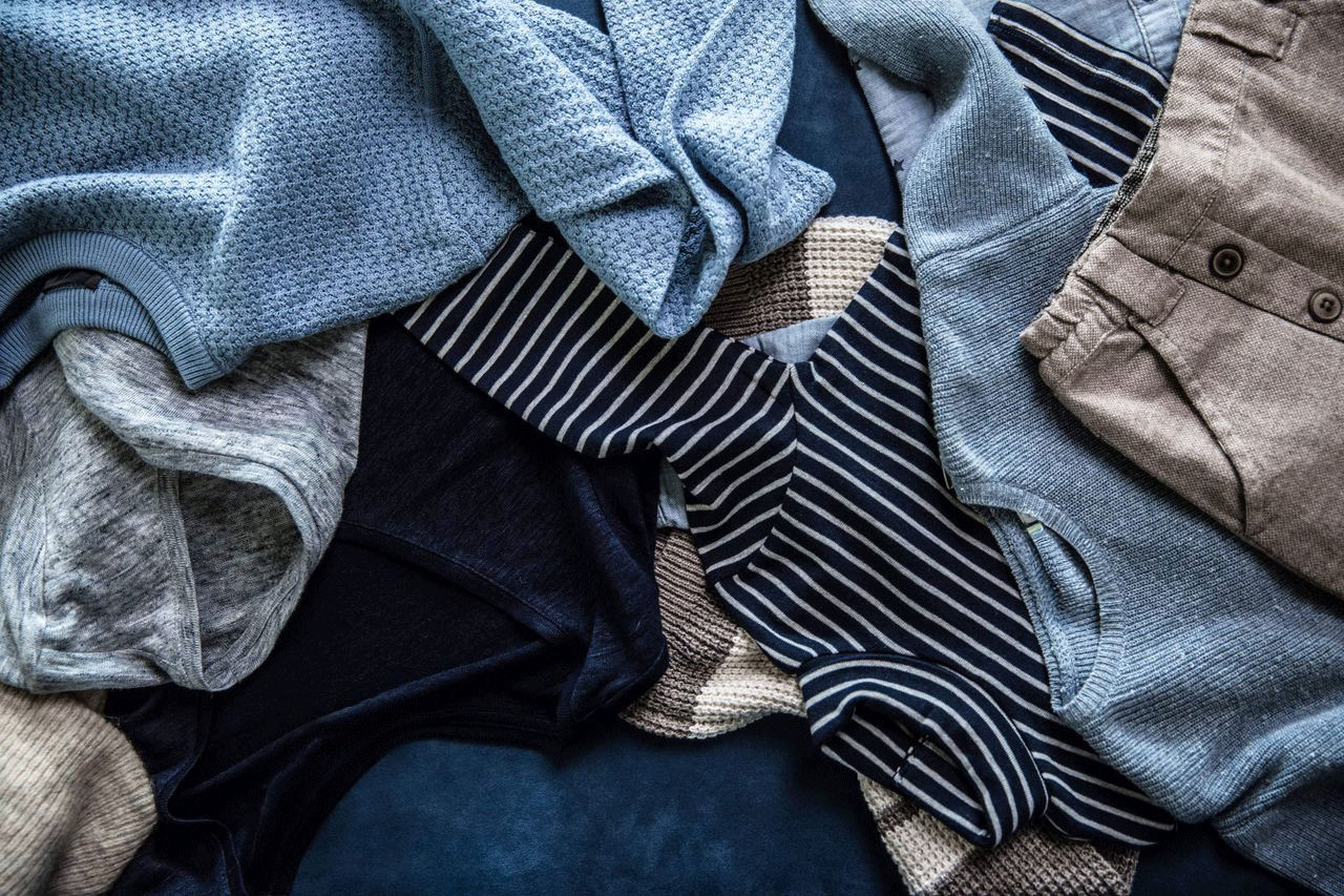 Verschiedene Kleidungsstücke, darunter blaue und gestreifte Pullover sowie eine blaue Hose, liegen übereinander.